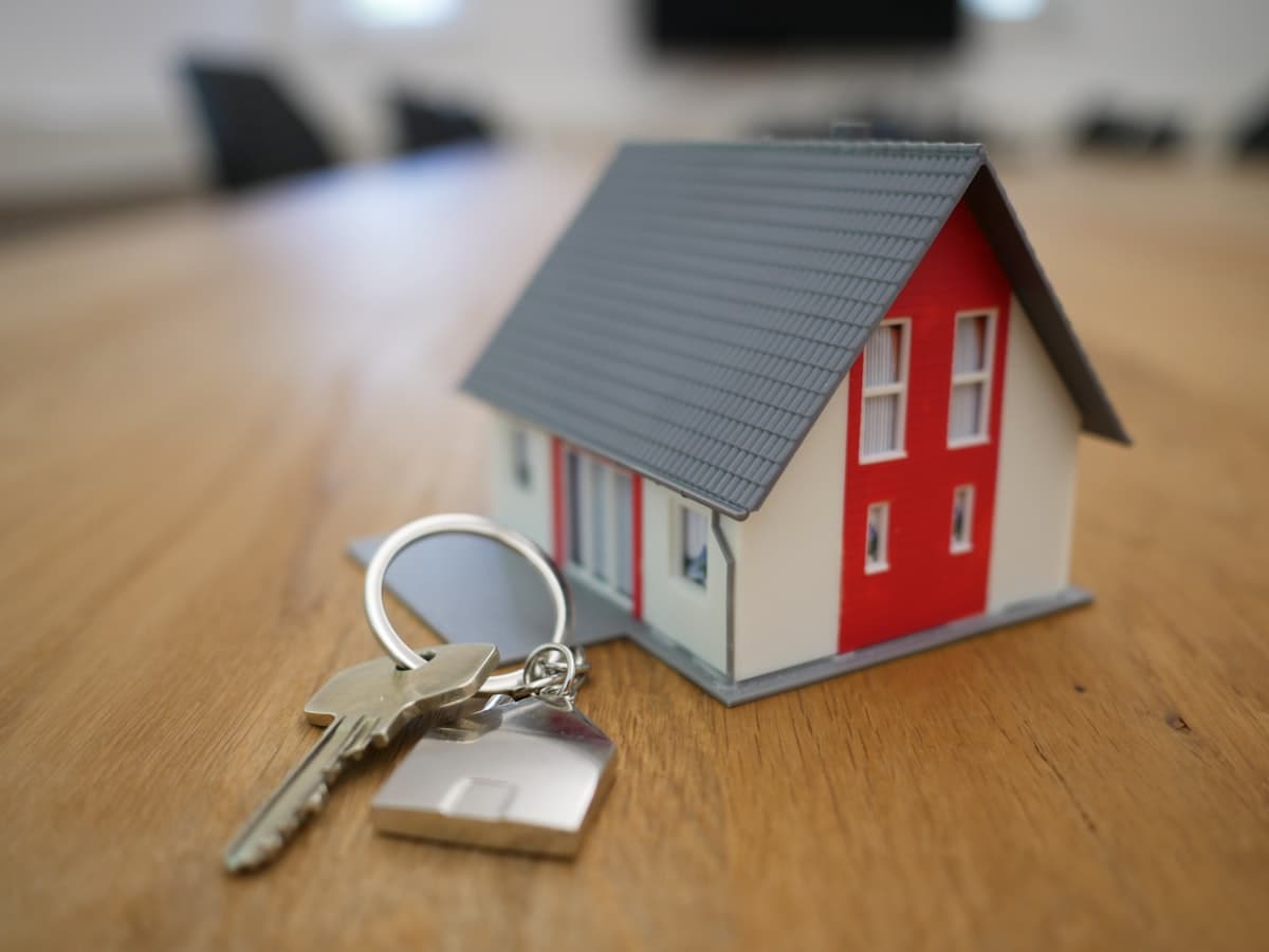 Hand holding a set of house keys in front of a new home